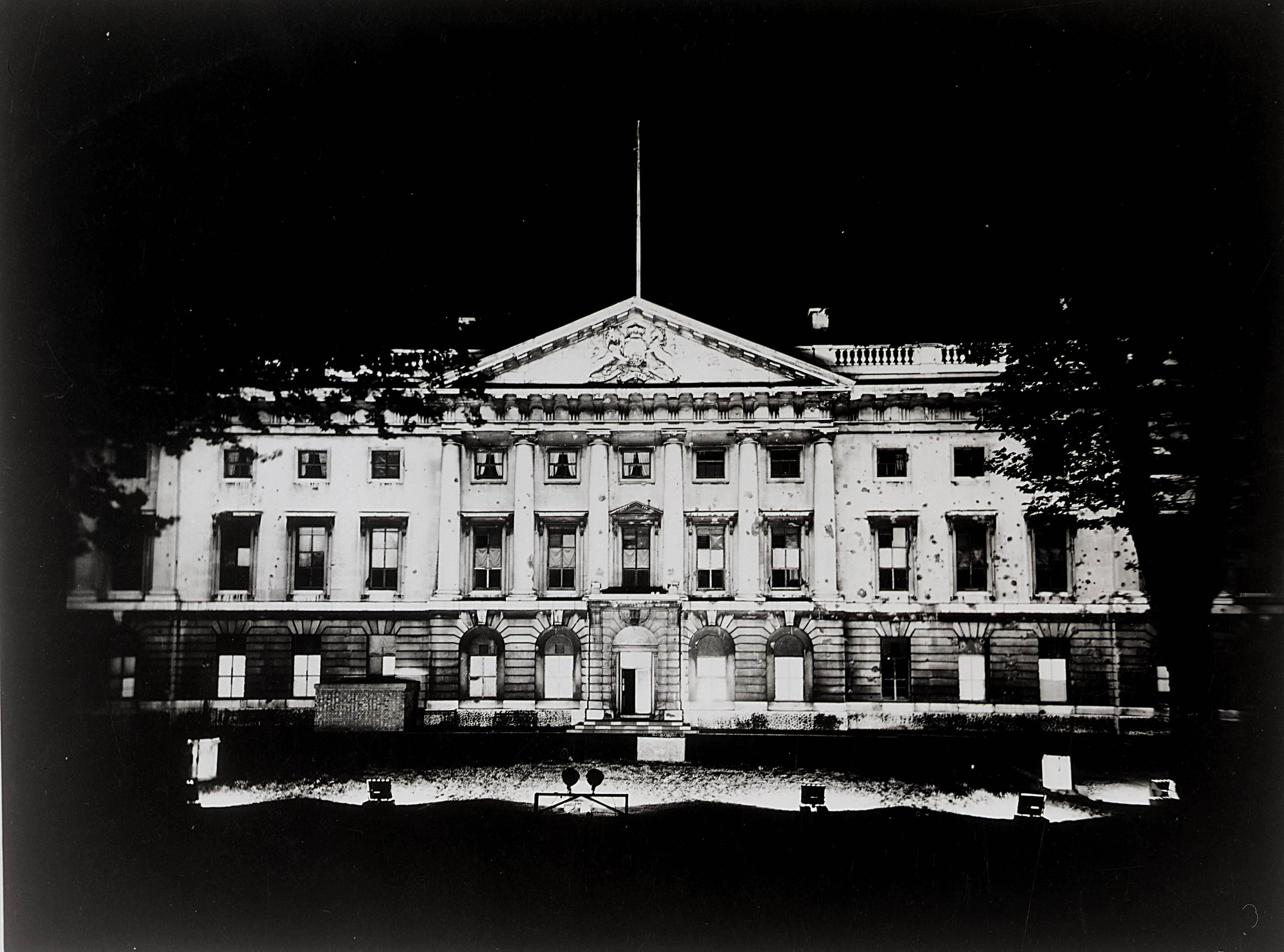 Royal Mint building at Tower Hill lit up on the night of V.E day showing bomb damage