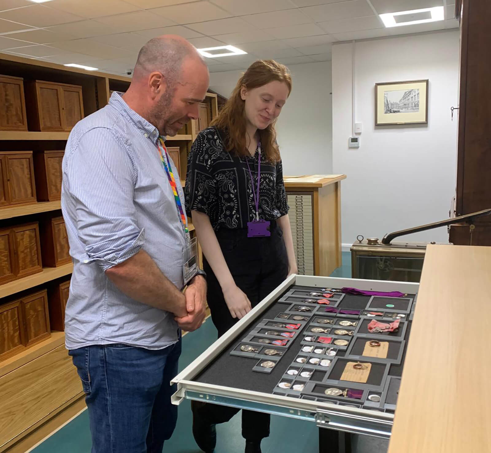 Two collections assistants stand looking at a tray of medals in the Royal Mint Museum