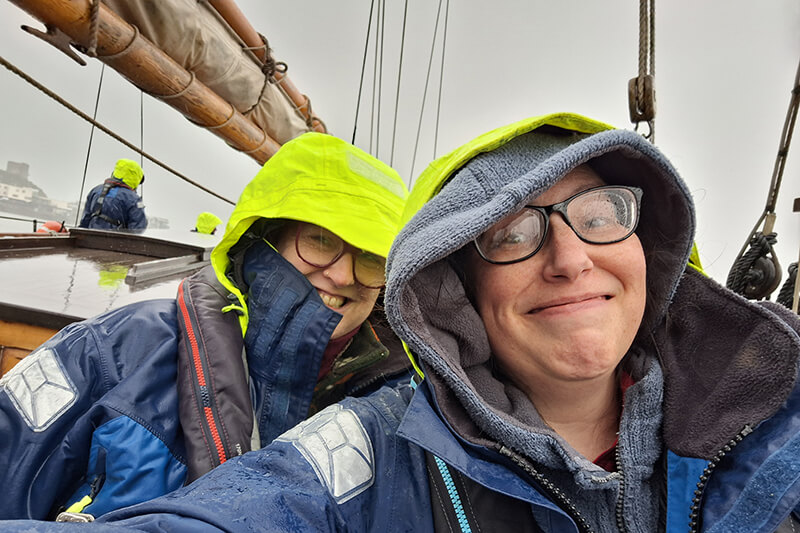 A selfie of the podcast team in waterproofs on board a sailing ship