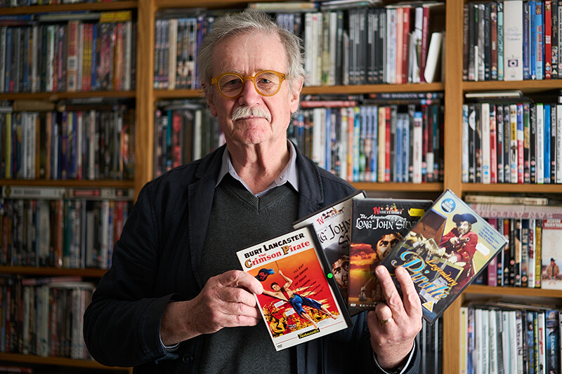 Sir Christopher Frayling holding a variety of DVDs of pirate films